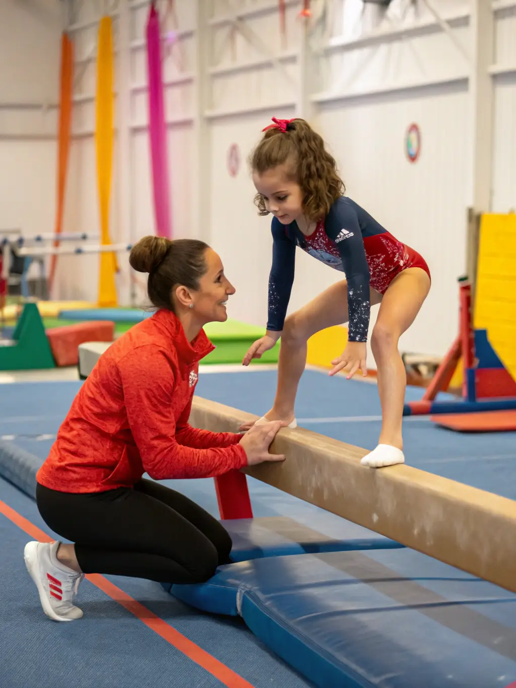 A focused image of a gymnastics instructor guiding a child through a specific exercise, emphasizing the personalized attention and expert guidance provided in the programs.